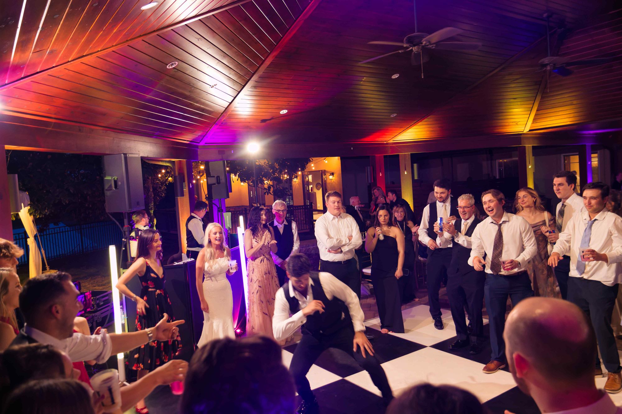 A checkered dance floor lit from above in purple and amber, guests watching from the edge