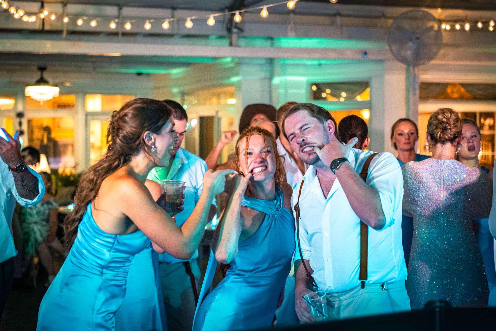 The same room again in teal, with guests dancing under the string lighting