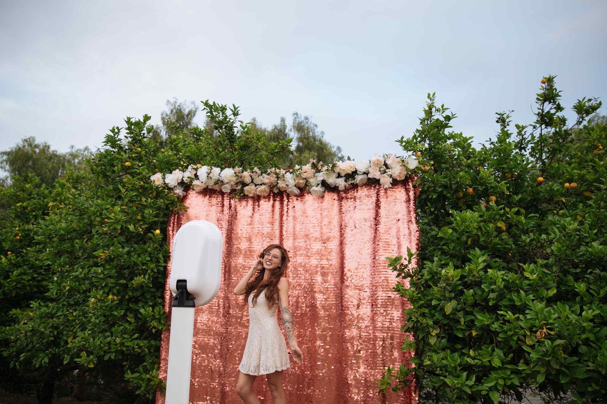 A guest laughing in front of a rose sequin backdrop and a flower garland, the open-air booth in the foreground