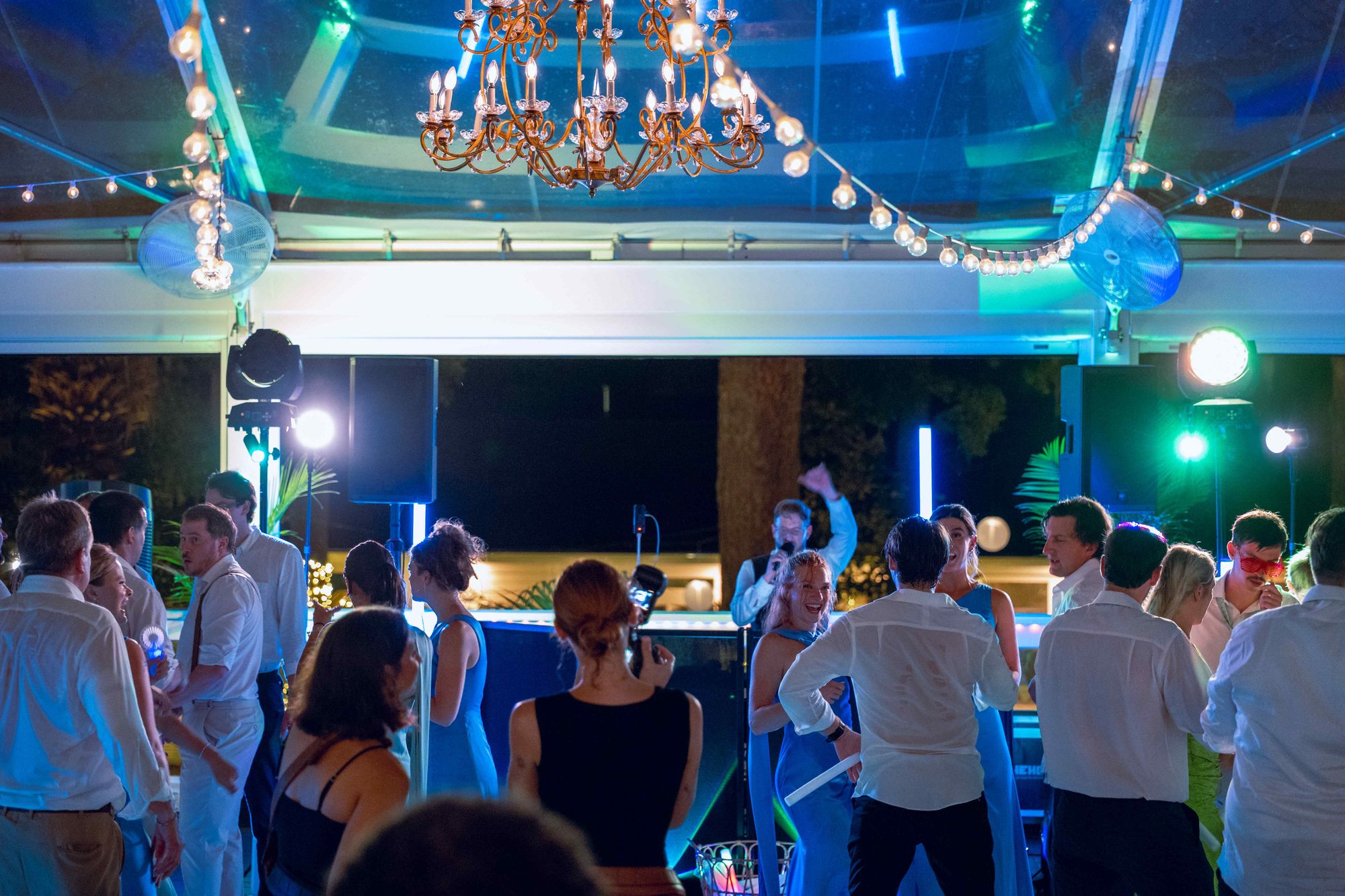 A marquee dance floor after dark under a chandelier and strings of warm light