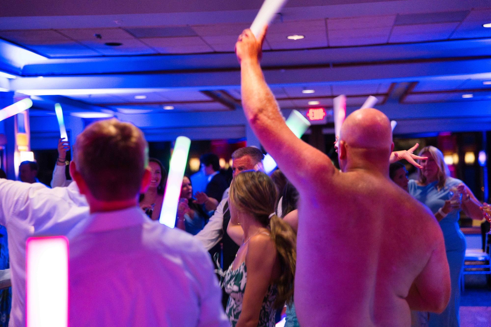 A crowded dance floor lit in blue, light sticks raised above the crowd