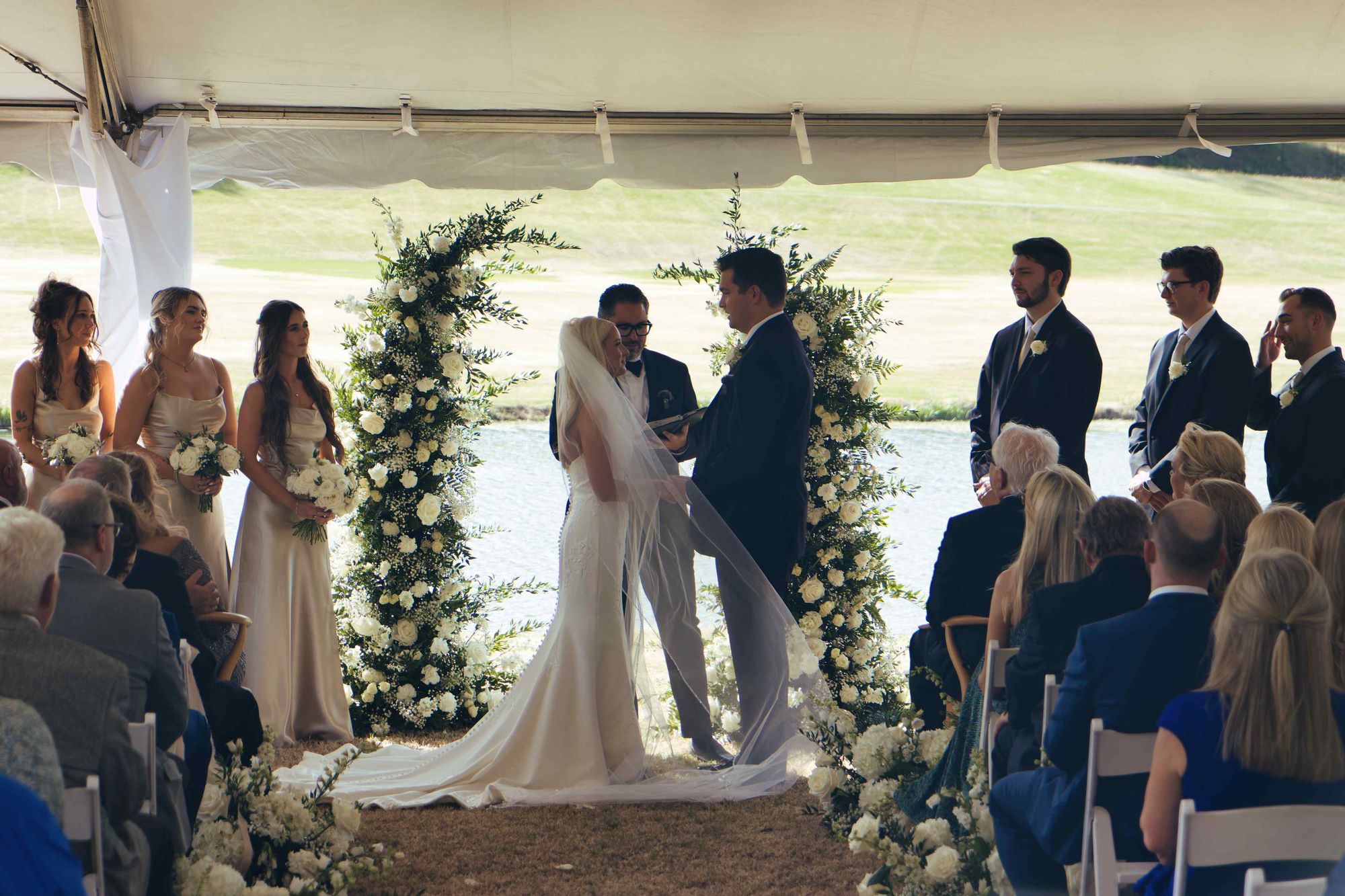 An outdoor ceremony under a marquee, a floral arch and the lake behind it