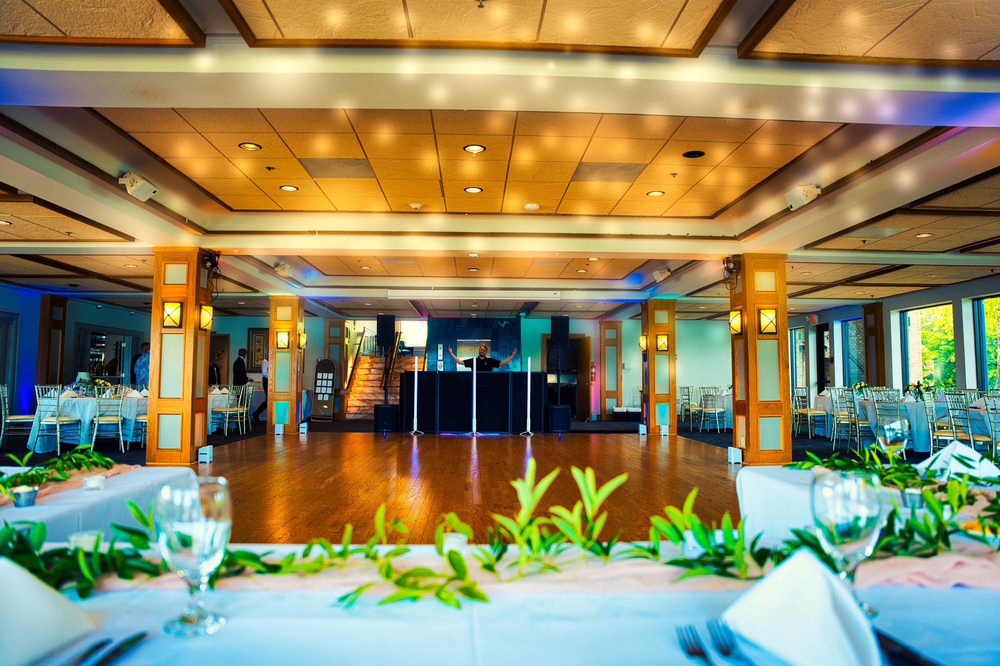 A reception room lit in teal and set for dinner, photographed before any guest has arrived